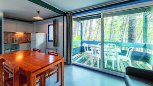 Una cocina moderna con una mesa y sillas de madera, un refrigerador y un comedor con vistas a un balcón y árboles.