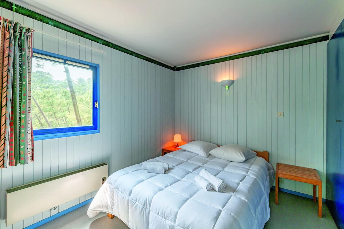 A bedroom with a bed, a window with curtains, a bedside table with a lamp, and a radiator.
