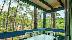 Un área de estar al aire libre techada, con una mesa y sillas, con vista a un paisaje boscoso.