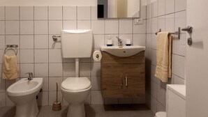 Une salle de bain comprenant des toilettes, un bidet, un lavabo, un miroir et un porte-serviettes.
