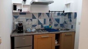 Une cuisine compacte équipée d’un réfrigérateur, d’une cuisinière et d’un évier. On y trouve des placards et un plan de travail sur lequel sont disposés divers objets.