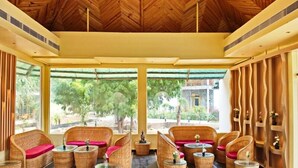 Un vaste espace intérieur aménagé avec des meubles en osier, de grandes fenêtres et un plafond en bois.