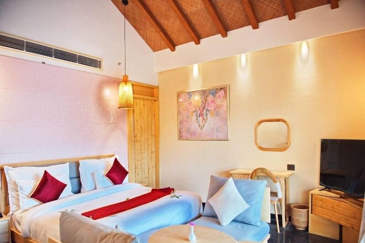 Habitación de hotel con cama, sofá, una mesita, televisor y un cuadro en la pared.
