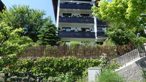 Un edificio de varios pisos con balcones, rodeado de vegetación y una cerca de madera.