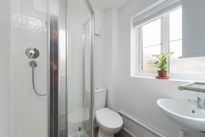 A bathroom with a glass-enclosed shower, a white toilet, a sink, and a window with a potted plant. - Milton Keynes Close to Station 6 bed Free Parking (Milton Keynes)