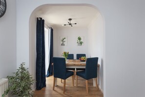 A dining area with a wooden table, four dark blue chairs, and a ceiling fan. - Milton Keynes Close to Station 6 bed Free Parking (Milton Keynes)