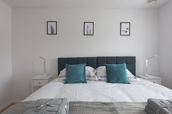 A neatly arranged bedroom with a large bed, two bedside tables, and three framed pictures on the wall. - Milton Keynes Close to Station 6 bed Free Parking (Milton Keynes)