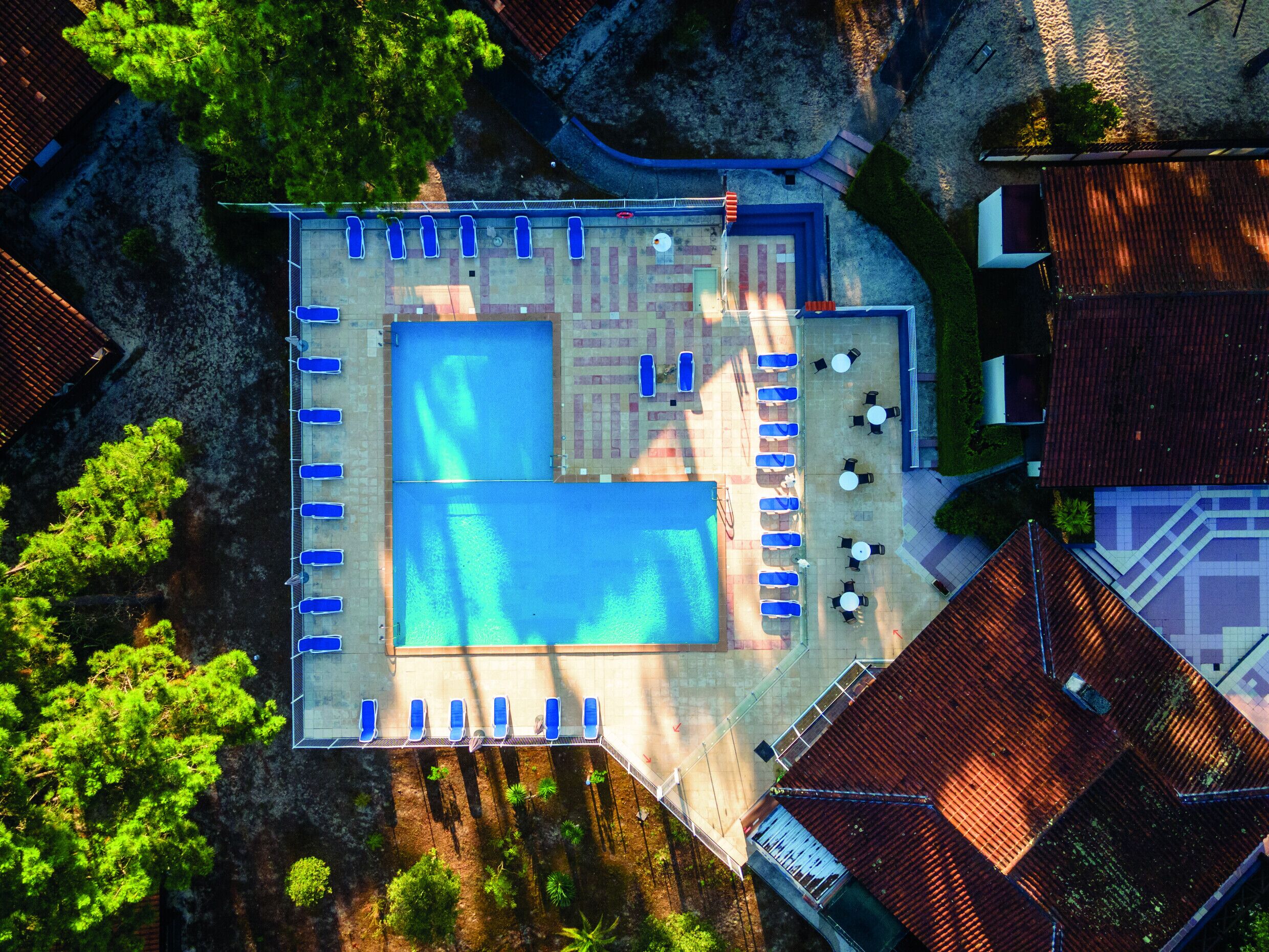 An aerial view of a resort with two swimming pools, sun loungers, and outdoor seating areas.