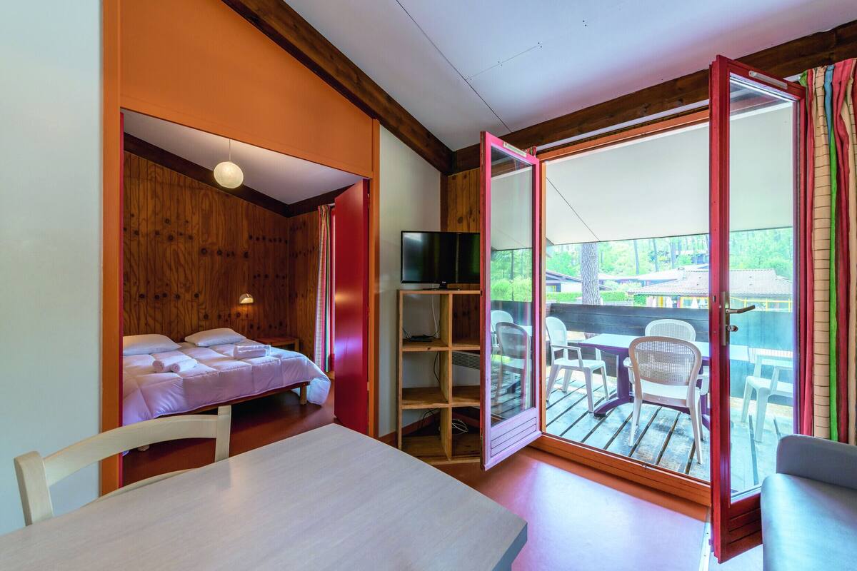 Un dormitorio con cama, televisor y puerta corrediza de vidrio que da a un patio exterior con sillas.