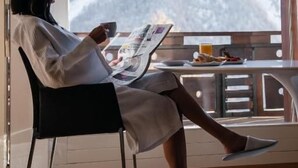Una persona sentada junto a una ventana con vistas a un paisaje nevado, leyendo un periódico.