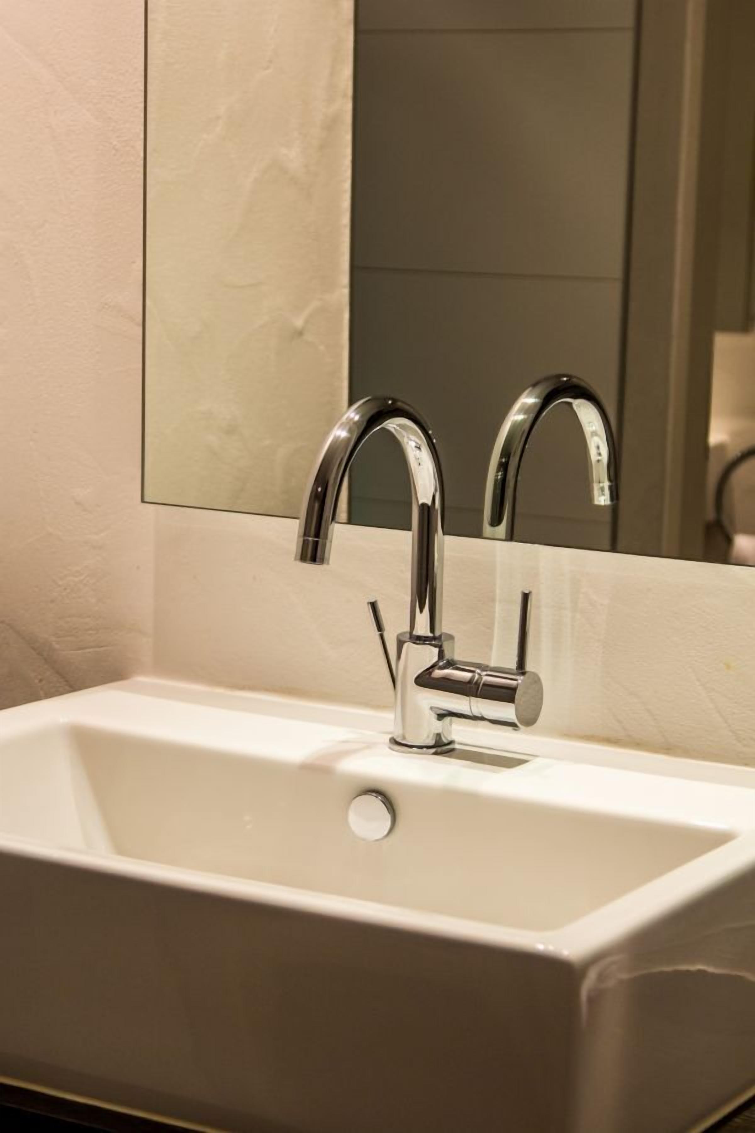 A bathroom with a white sink, two chrome faucets, and a mirror above it.