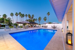 A swimming pool with lounge chairs and umbrellas, surrounded by palm trees and a building with outdoor seating. - ⚓Sleeps 23! 2 Houses on 1 Acre, Min to AMI Beaches!⚓⛳ (Bradenton)