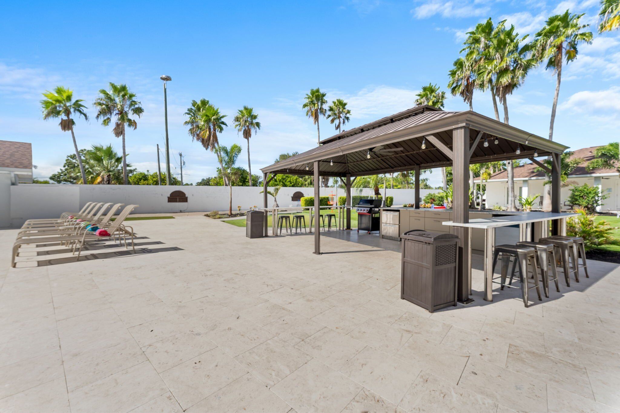 Une terrasse extérieure dotée d’un espace barbecue couvert, de chaises longues et d’un bar avec des tabourets.