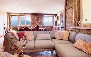 A modern living room with a sectional sofa, wooden walls, and large windows offering mountain views.