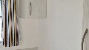 Un dormitorio con una cama blanca, una cortina a rayas y un armario blanco con pomo.