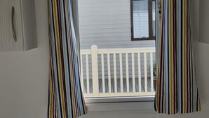 Una habitación con cama, una ventana con cortinas a rayas, vista a un balcón y una pared blanca con un armario.