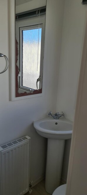 Een kleine badkamer met een wit wastafel, een raam met metalen frame en een radiator.