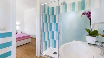 A modern bathroom with a glass shower enclosure, a white sink, and a bed with a striped bedspread.
