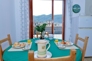 Una mesa de comedor lista para el desayuno, una planta en maceta y vistas a edificios y colinas a través de una ventana.