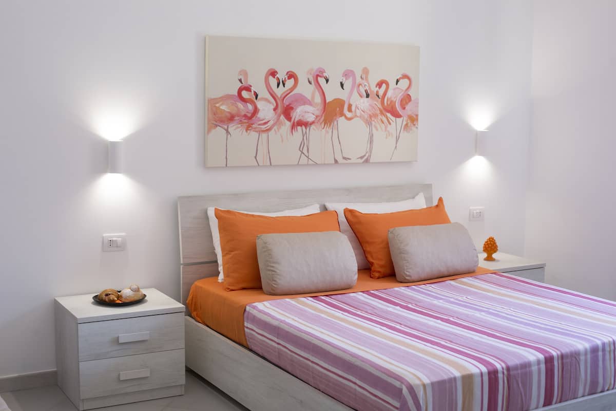 Un dormitorio con cama, mesitas de noche y un cuadro de flamencos.