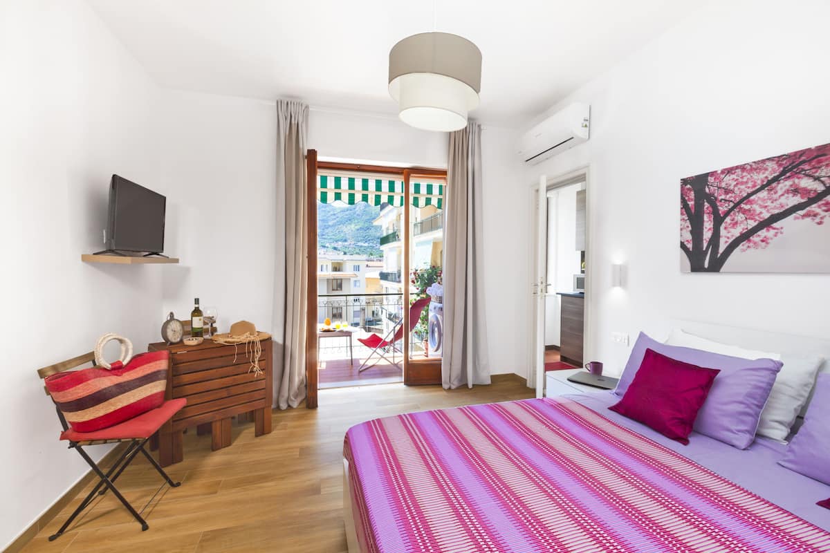 Un dormitorio con cama, escritorio, silla, televisor y vistas al exterior.