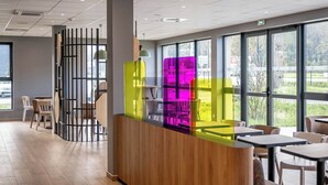 A modern interior with a reception desk, seating area, and large windows offering a view of the outdoors. - B&B HOTEL Bordeaux Saint André De Cubzac (Saint-André-de-Cubzac)