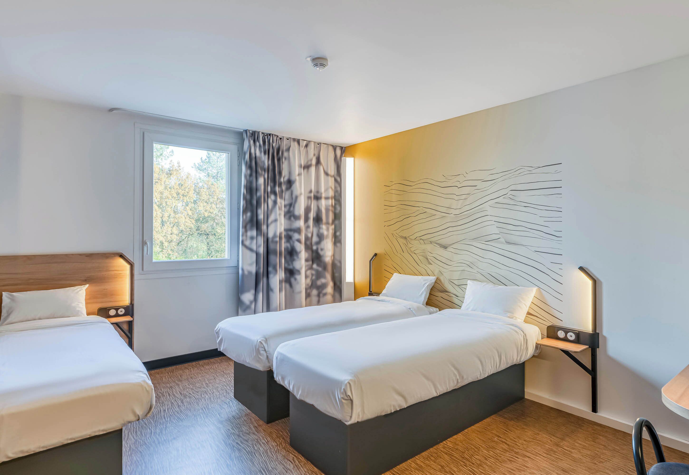 Ein Hotelzimmer mit zwei Betten, einem großen Fenster mit Vorhängen, einem modernen Wandbild und einer Deckenleuchte.
