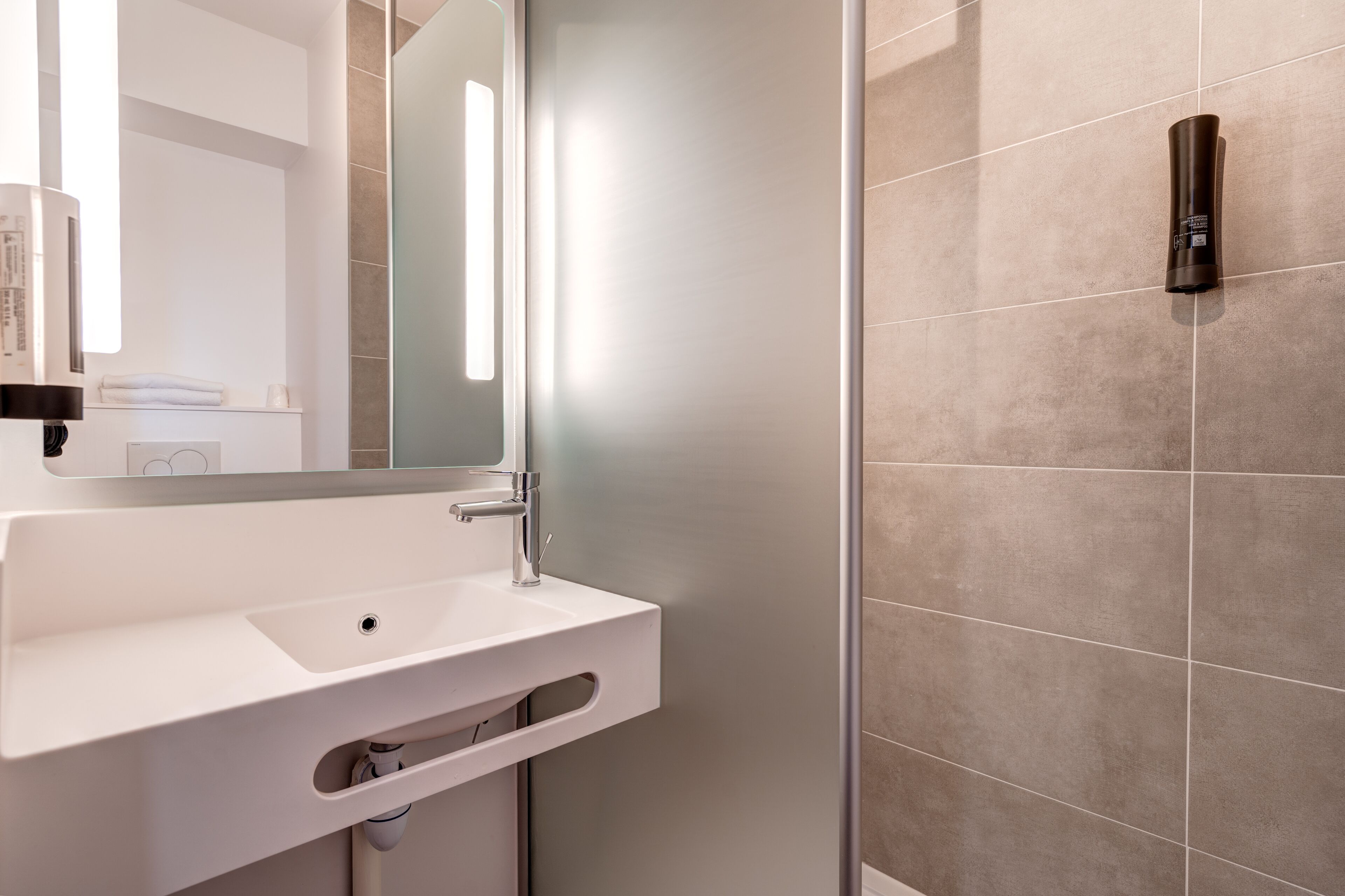 A modern bathroom with a white sink, a large mirror, and a wall-mounted light fixture.