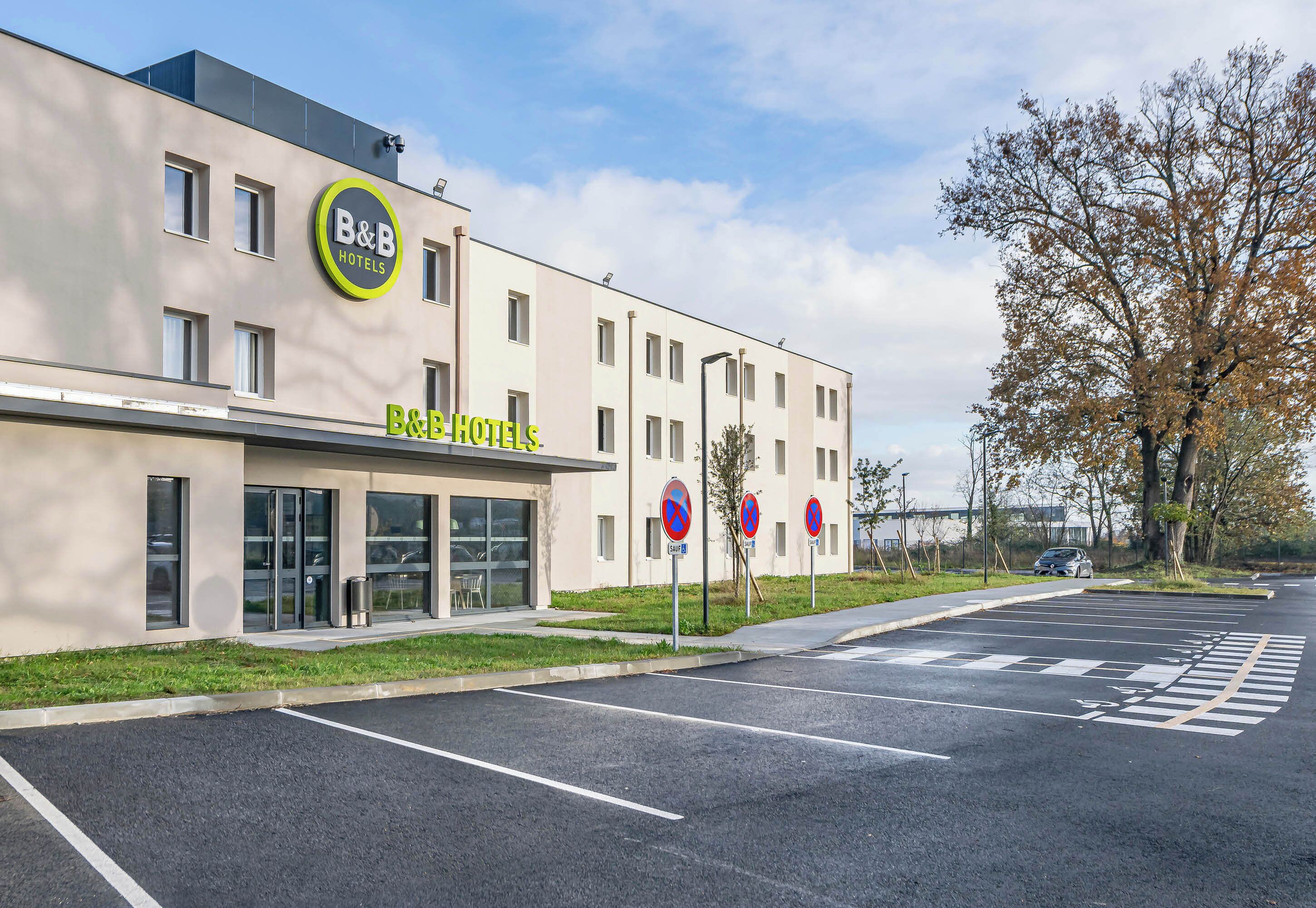 A B&B hotel building with a modern facade, multiple windows, and a parking lot with no parking signs.