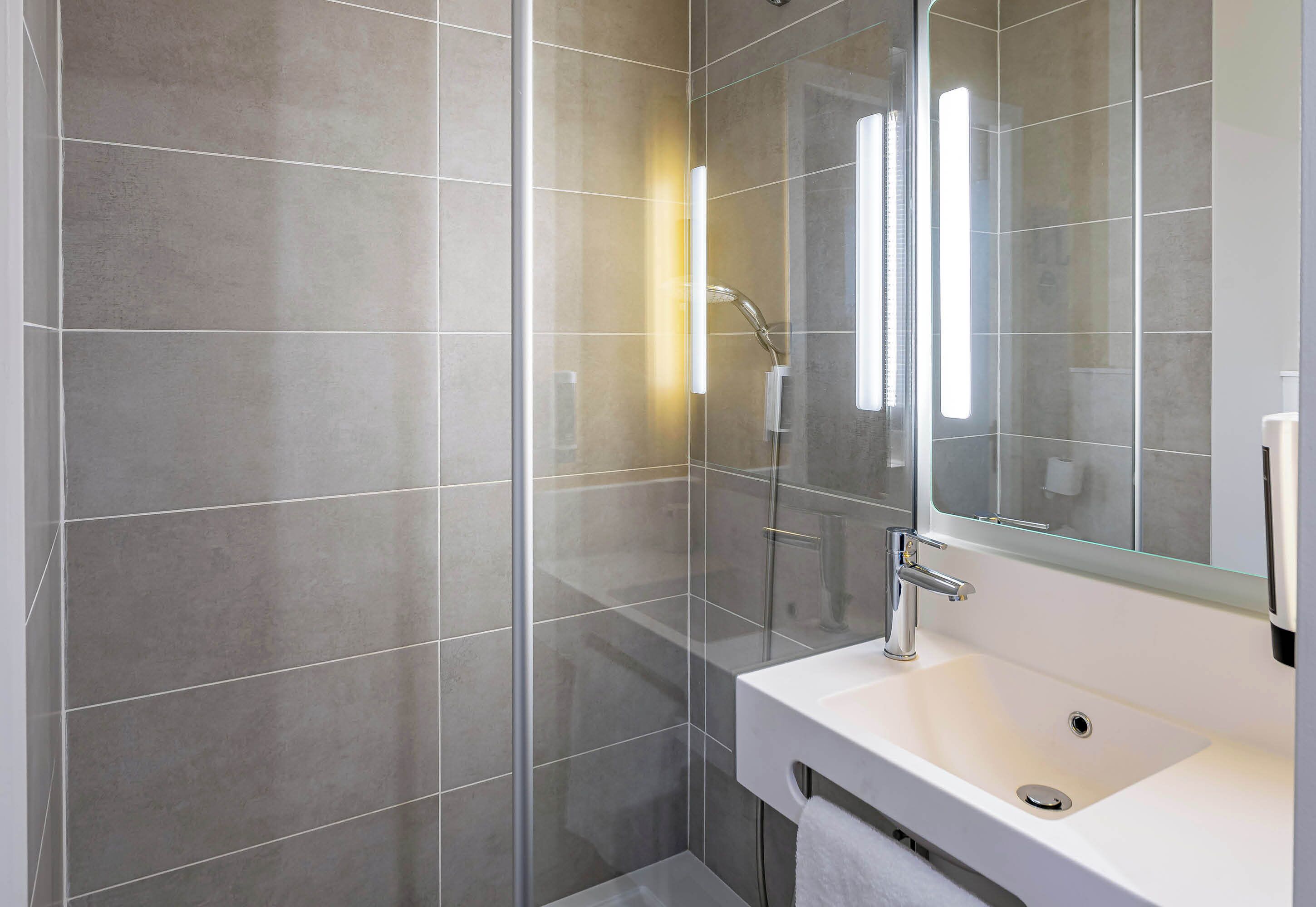 A modern bathroom with a glass-enclosed shower, a white sink, and a large mirror.