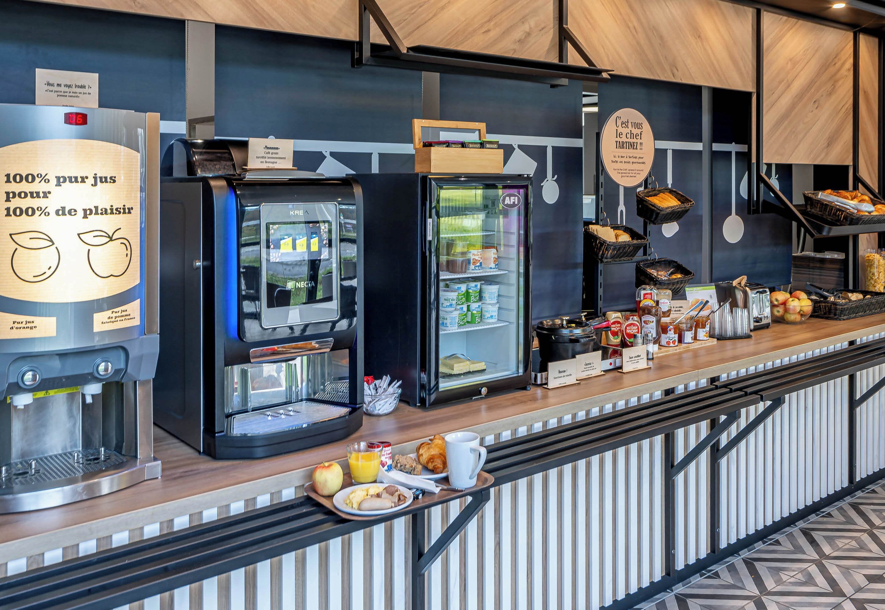 Una barra de desayuno con cafetera, refrigerador y una variedad de alimentos.