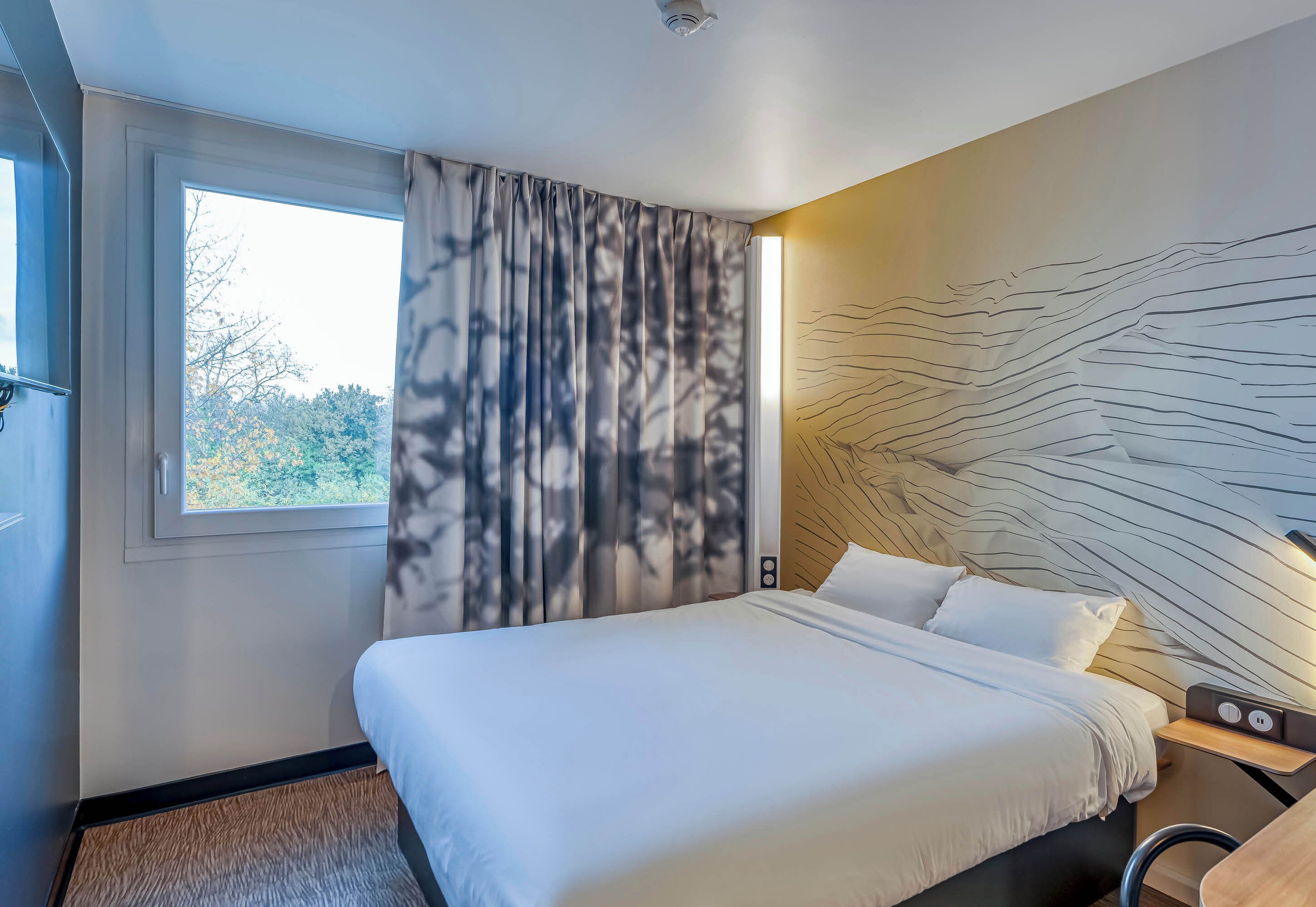 Quarto de hotel com uma cama grande, janela com cortinas e parede com design texturizado.