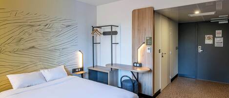 Habitación de hotel con una cama grande, un escritorio con silla, perchero y armario.