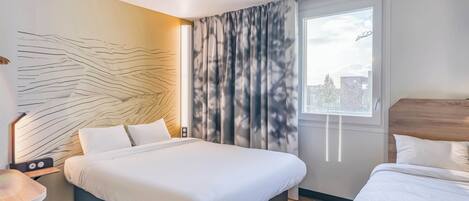 A modern hotel room with a large bed, a bedside table with a lamp, and a view of the city through a window with curtains.