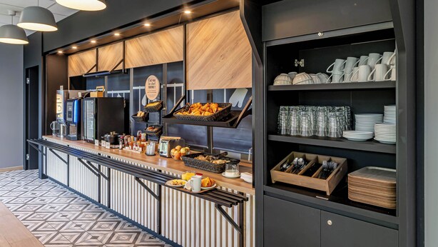 A modern breakfast bar with a variety of food items, a coffee machine, and neatly arranged dishes and utensils. - B&B HOTEL Bordeaux Saint André De Cubzac (Saint-André-de-Cubzac)