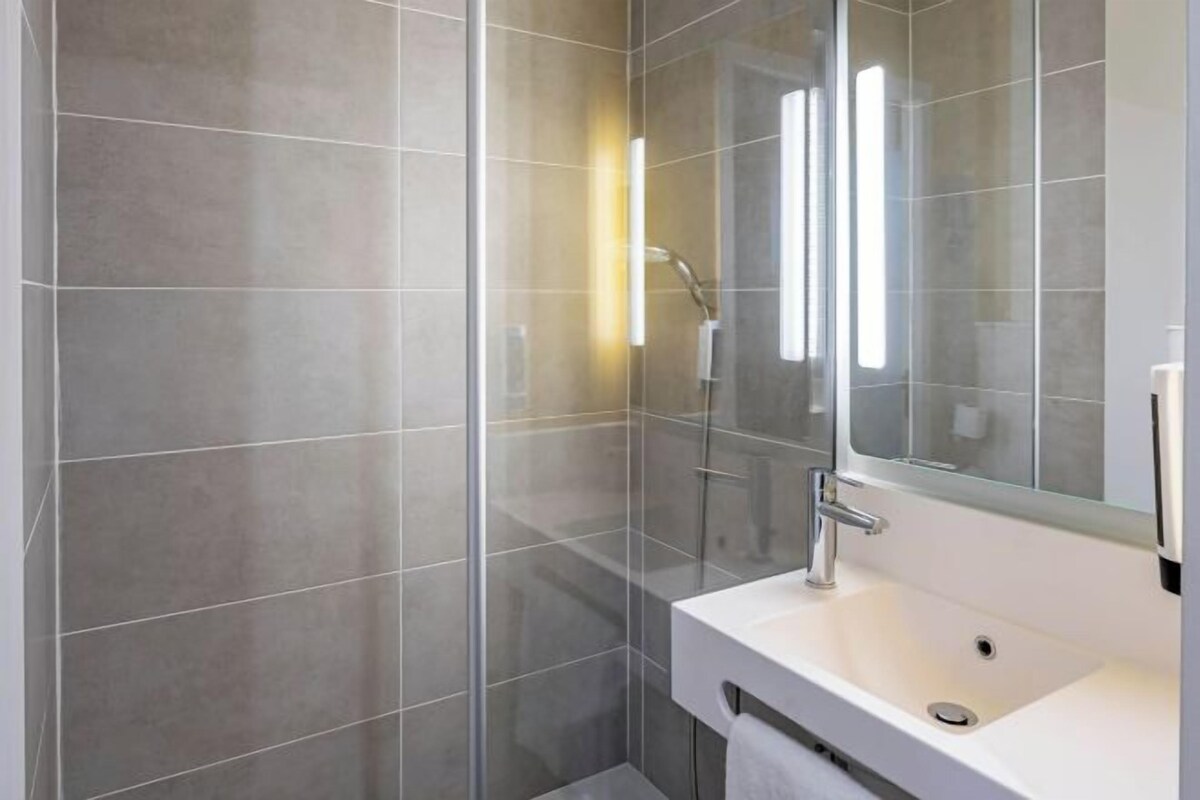 A modern bathroom with a glass shower enclosure, a white sink, and a large mirror.