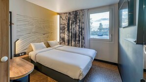 A modern hotel room with a double bed, a small bedside table, a wall-mounted TV, and a window with curtains. - B&B HOTEL Bordeaux Saint André De Cubzac (Saint-André-de-Cubzac)