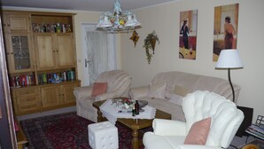 A living room with a beige sofa, a white armchair, a coffee table, and a bookshelf filled with books. - Apartment on the 1st floor. Only 10 minutes walk to the town center. (Berchtesgaden)