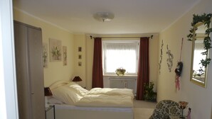 A bedroom with a bed, a chair, a small table, a radiator, a window with curtains, and a door. - Apartment on the 1st floor. Only 10 minutes walk to the town center. (Berchtesgaden)