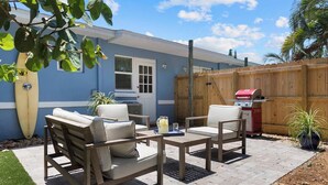 A patio with two beige cushioned chairs, a small table, and a barbecue grill.
