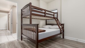 Ein Stockbett mit Holzrahmen und weißer Bettwäsche in einem Zimmer mit hellem Holzboden und weißen Wänden.