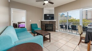 Ein Wohnzimmer mit Sofa, Sessel, Couchtisch, Kamin, Fernseher und einem Balkon mit Sitzgelegenheiten.