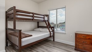 A bunk bed in a room with a window, a dresser, and a white wall.