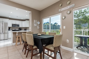 A modern kitchen with white cabinets, a microwave, and a coffee maker. There is a dining table with chairs and a black tablecloth. The room has a large window with a view of buildings and trees. - Princess Irene Unit 202 Oceanside 3BR 2BathCondo +Jacuzzi and parking (Ocean City)