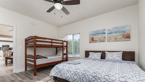 A bedroom with a bunk bed, a large bed with patterned bedding, a ceiling fan, and beach-themed wall art. - Princess Irene Unit 202 Oceanside 3BR 2BathCondo +Jacuzzi and parking (Ocean City)