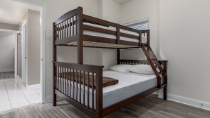 Een stapelbed in een kamer met een deur naar een andere kamer en een raam met jaloezieën.