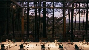 A dining table set for a meal with candles, glasses, and plates, set against a backdrop of trees and a mountainous landscape. - Mơ Stay Forest Resort (Xuan Huong - Da Lat)