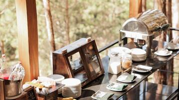Un buffet de petit-déjeuner est installé sur une table en verre, dans un espace boisé, et propose une variété d’aliments et de boissons en libre-service.