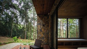 A wooden deck with a stone wall, a bench, and a view of a forest. - Mơ Stay Forest Resort (Xuan Huong - Da Lat)