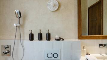 A modern bathroom with a shower, three black soap dispensers, a small bowl, and a towel on the counter.